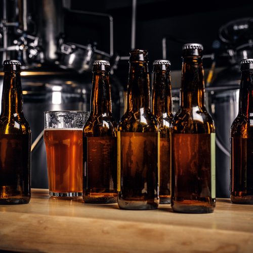 Bottles and glass of craft beer on wooden bar counter at indie brewery.